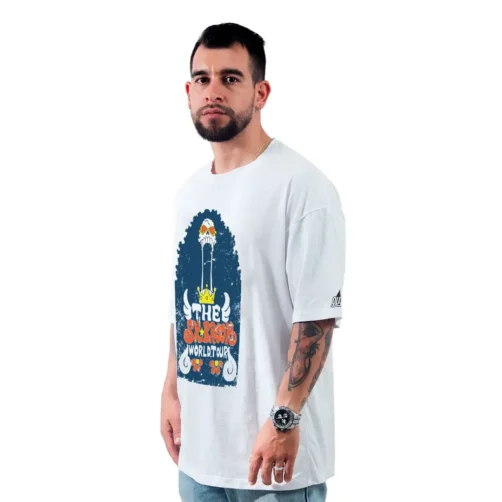 Un hombre está parado sobre un fondo blanco, vistiendo una camiseta gráfica blanca con el texto "The Blessing World Tour", que irradia vibraciones retro geniales que se hacen eco de los estilos clásicos de la cultura pop.