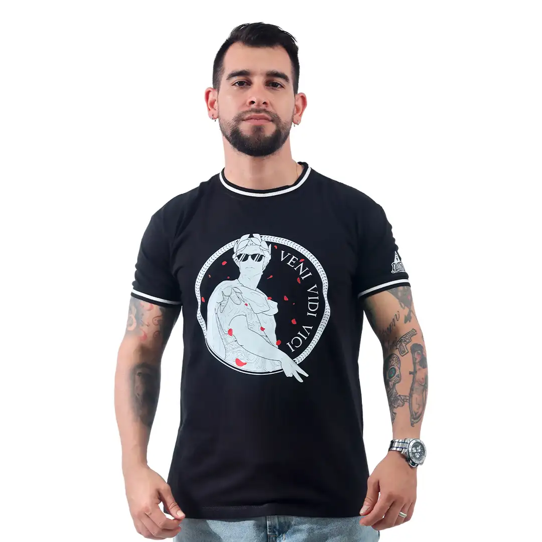 Un hombre de pie con los brazos a los costados, vistiendo la camiseta negra Julio César Pop Art - Camiseta Cuello Tejido, que presenta un diseño gráfico y el texto "Veni Vidi Vici". Esta camiseta personalizada resalta sus tatuajes y un reloj en su muñeca izquierda, combinando a la perfección el estilo con la expresión personal.
