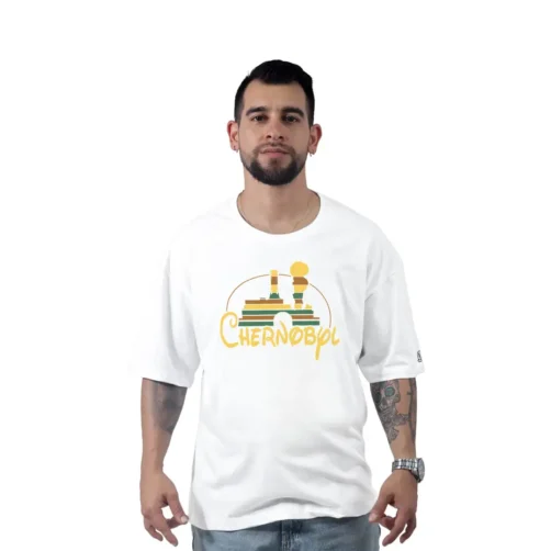 Un hombre aparece de pie sobre un fondo blanco liso, con una camiseta extragrande de Chernobil/Disney de la serie Estilos. La camiseta está adornada con un diseño de reactores nucleares, que transmite un aire retro que llama la atención sin esfuerzo.
