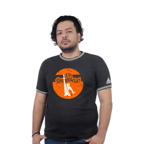Una persona viste la camiseta "Espartaco en la cima - Camiseta Cuello Tejido", que muestra una camiseta negra con un gráfico naranja con la frase "Soy Espartaco" acompañado de un diseño de dibujos animados en el frente, combinando a la perfección elementos de los estilos de la cultura pop.