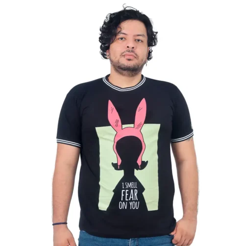 Un hombre lleva una camiseta negra "I Smell Fear On You de Louise" de la serie Estilos, que presenta la frase "I smell fear on you" junto con peculiares orejas de conejo rosas, combinando estilo y humor a la perfección.