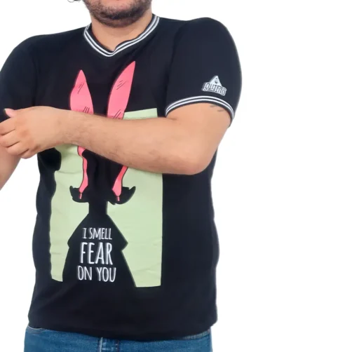 Una persona que viste la camiseta "I Smell Fear On You de Louise", con su escote tejido y su llamativo diseño de piernas rosas combinadas con el texto en negrita, irradia un estilo creativo que combina sin esfuerzo con las influencias de la cultura pop.