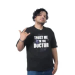 Una persona con cabello rizado en una Tardis de Doctor Who - Camiseta Oversized negra, con las palabras "Confía en mí, soy el doctor", canaliza a Estilos Gamer mientras gesticula con una mano.