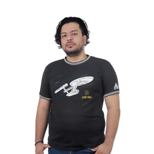 Una persona viste la USS Enterprise (NCC-1701) - Camiseta Cuello Tejido, que presenta un diseño de nave espacial con estilos retro, de pie sobre un fondo blanco liso.
