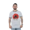 Un hombre que viste una camiseta blanca con un gráfico y texto en rojo se encuentra sobre un fondo blanco, mostrando su estilo de jugador único.