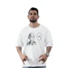 Una persona con barba que viste una camiseta personalizada, que muestra un personaje de dibujos animados y la palabra "OK" en estilos de anime, posa sobre un fondo blanco liso.