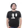 Una persona que viste una camiseta negra con la imagen de un personaje de cómic en estilo anime que dice "OK" está parada sobre un fondo blanco.