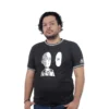 Una persona está de pie sobre un fondo blanco, vistiendo una camiseta negra que encarna estilos de cultura pop, con un personaje de cómic junto al texto "OK.