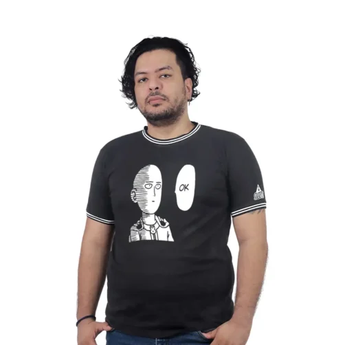 Una persona está de pie sobre un fondo blanco, vistiendo una camiseta negra que encarna estilos de cultura pop, con un personaje de cómic junto al texto "OK.