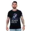 Un hombre que viste la camiseta "John Wick - Camiseta Cuello Tejido" en color negro, que muestra un gráfico retro del personaje sosteniendo un perro, se encuentra con una expresión neutra.