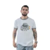 Un hombre con barba, que viste una camiseta blanca de "Miedo y asco en Las Vegas" y jeans, imita estilos retro mientras permanece de pie frente a un fondo blanco liso.