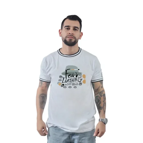 Un hombre con barba, que viste una camiseta blanca de "Miedo y asco en Las Vegas" y jeans, imita estilos retro mientras permanece de pie frente a un fondo blanco liso.