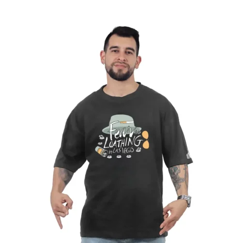 Una persona con una camiseta negra con un diseño gráfico que dice "Miedo y asco en Las Vegas" muestra su estilo retro, posando sobre un fondo blanco liso.