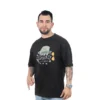 Un hombre tatuado con barba viste la camiseta "Fear and Loathing in Las Vegas - Camiseta Oversized", con un diseño y texto retro, mientras señala con seguridad con su mano derecha.