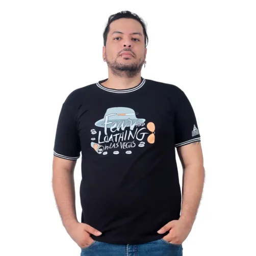 Una persona se para con confianza sobre un fondo blanco, vistiendo la Camiseta Cuello Tejido que presenta un gráfico y un texto que dice "Miedo y asco en Las Vegas", que rezuma estilos de anime.