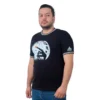 Un hombre que viste la camiseta "Dedo E.T. - Camiseta Cuello Tejido", que presenta un diseño de silueta iluminada por la luna, se encuentra sobre un fondo blanco liso, que representa estilos de cultura pop.
