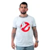Un hombre con tatuajes, que encarna estilos retro, viste una camiseta blanca de Los Cazafantasmas mientras está de pie mirando hacia adelante.