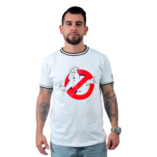 Un hombre con tatuajes, que encarna estilos retro, viste una camiseta blanca de Los Cazafantasmas mientras está de pie mirando hacia adelante.