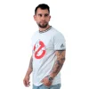 Un hombre con tatuajes viste una camiseta blanca de Los Cazafantasmas y unos vaqueros, encarnando a Estilos Gamer mientras mira hacia un lado contra un fondo liso.