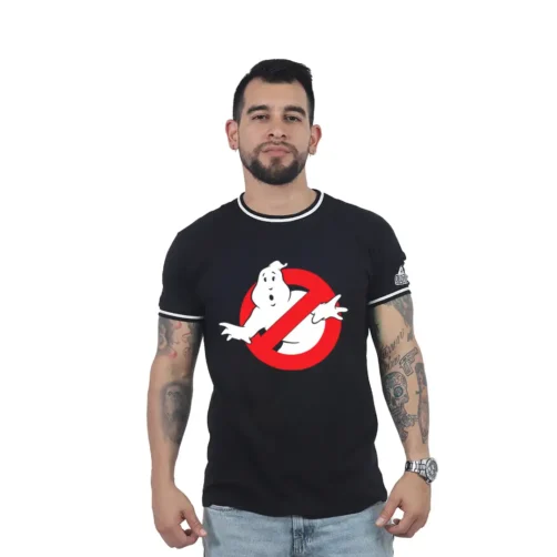 Un hombre con una camiseta negra de Los Cazafantasmas se yergue con seguridad sobre un fondo blanco liso. Sus brazos lucen intrincados tatuajes que le añaden un toque retro a su look.