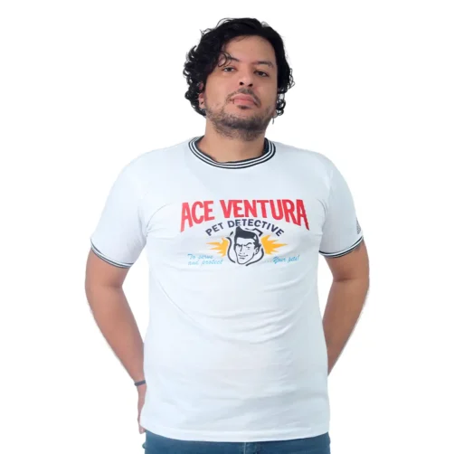 Una persona que viste una camiseta blanca con la leyenda "Ace Ventura Pet Detective" y un dibujo en el frente, parada sobre un fondo liso, transmite vibraciones retro de estilos sin esfuerzo.