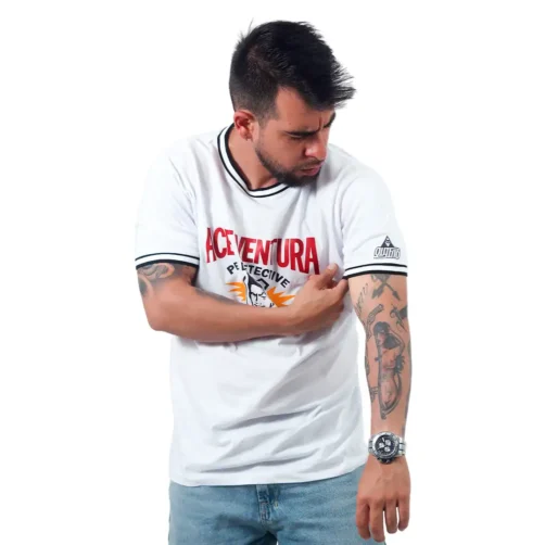 Un hombre con una camiseta blanca con texto impreso inspecciona su brazo tatuado, mostrando diseños inspirados en estilos de anime.