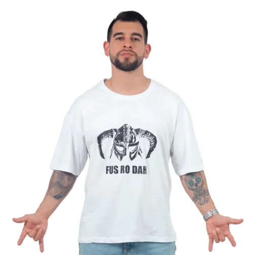 Un hombre barbudo que viste la camiseta Fus Ro Dah de Skrim - Oversized, que muestra un gráfico de un casco con cuernos y el texto "FUS RO DAH", está de pie con las manos ligeramente abiertas.