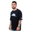Un hombre que viste una camiseta negra "Meme de Gatita - Camiseta Oversized" con un diseño de gato de dibujos animados se para con confianza sobre un fondo blanco.