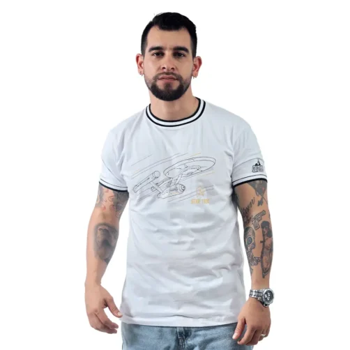 Un hombre con tatuajes viste casualmente una camiseta blanca personalizada de Star Trek "USS Enterprise (NCC-1701) - Camiseta Cuello Tejido", combinada con jeans claros, de pie sobre un fondo blanco liso.