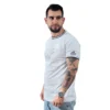 Un hombre con tatuajes, abrazando a Estilos Gamer, viste la USS Enterprise (NCC-1701) - Camiseta Cuello Tejido junto con unos jeans. Mira hacia un lado contra un fondo liso.