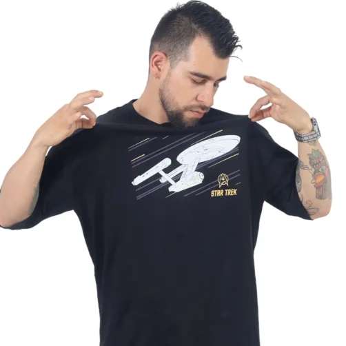 Un hombre que viste una camiseta enorme del USS Enterprise (NCC-1701), que evoca estilos retro, sostiene el cuello con ambas manos mientras mira hacia abajo pensativamente.