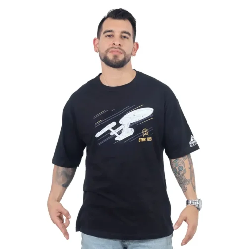 Un hombre con una camiseta negra de gran tamaño del USS Enterprise (NCC-1701) con un gráfico de una nave espacial la combina con jeans y está parado con los brazos ligeramente abiertos.