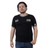 Una persona con cabello ondulado, vestida con un Logo de Sons of Anarchy - Camiseta Cuello Tejido y jeans azules, se encuentra sobre un fondo blanco liso, encarnando la esencia de la cultura pop.