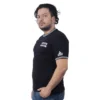 Un hombre de cabello oscuro y barba se encuentra de pie en el "Logotipo de Sons of Anarchy - Camiseta Cuello Tejido", que presenta un texto blanco en negrita que representa estilos de anime. Mira ligeramente hacia la cámara contra un fondo blanco liso, capturando una atmósfera relajada y relajada.
